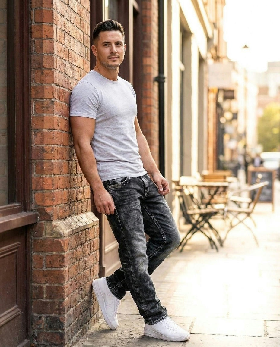 Man wearing Rufus relaxed straight-leg jeans in black, leaning on a brick wall